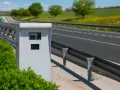 Caja blanca de nuevos radares DGT junto a una carretera con guardarraíl y campo verde al fondo.