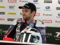 William Dunlop, piloto de motociclismo, sonríe con su casco de carreras y mono de competición.