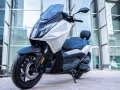 Scooter Mitt 330 GTS blanco y negro, con ABS, aparcado frente a un edificio moderno. ¡Sin problemas para disfrutar!