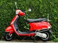 Scooter roja aparcada frente a un seto verde. Ideal para entender las diferencias carnet a1 y a2.