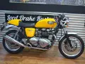 Motocicleta Triumph Thruxton 900 amarilla, estilo café racer, lista para la carretera.