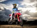Jett Lawrence, piloto de motocross, posa con su moto roja bajo un cielo dramático.