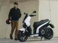 Hombre con casco junto a un scooter eléctrico blanco, el scooter mas potente para la ciudad.