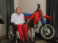 Andre Malherbe, leyenda del motocross, sonríe junto a su icónica moto Honda roja.