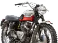 Clásica moto Triumph, modelo scrambler, con tanque bicolor rojo y blanco, motor expuesto y llantas todoterreno.