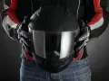 Persona con guantes de moto sostiene casco negro. Se aprecian detalles de las medidas exteriores casco moto en su diseño.