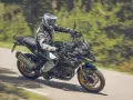 Motociclista con equipo de protección conduce una de las motos trail media cilindrada por una carretera rodeada de vegetación.