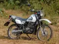 Suzuki DR 200 lista para la aventura. Moto blanca de doble propósito con neumáticos todoterreno, lista para explorar caminos rurales.