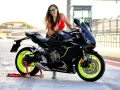 Chica sonriente con gafas verdes posa junto a una moto Honda CBR negra con detalles neón, perfecta para motos r para el a2.