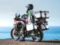Motociclista con equipaje de **marca Kappa** listo para la aventura junto al mar.