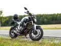 Una moto a2 blanca y negra, con un casco negro en el asiento, aparcada en la cuneta de una carretera rural.