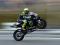 Valentino Rossi levanta la rueda trasera de su Yamaha en plena carrera, con su icónico casco amarillo y traje azul.