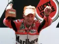Ralf Waldmann, piloto de motos, celebra con un trofeo y un puño en alto, luciendo su traje de competición Marlboro.