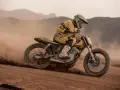 Piloto con casco y traje amarillo compite en una moto por una **dirt track**, levantando polvo en un paisaje desértico.