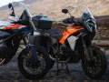 Dos motos KTM Super Adventure listas para la aventura. Modelos naranjas y blancos, con maletas, en un paisaje árido.