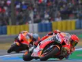 Dos pilotos de long lap motogp se inclinan en una curva, con el público borroso al fondo.