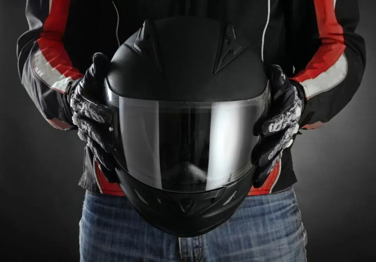 Persona con guantes de moto sostiene casco negro. Se aprecian detalles de las medidas exteriores casco moto en su diseño.