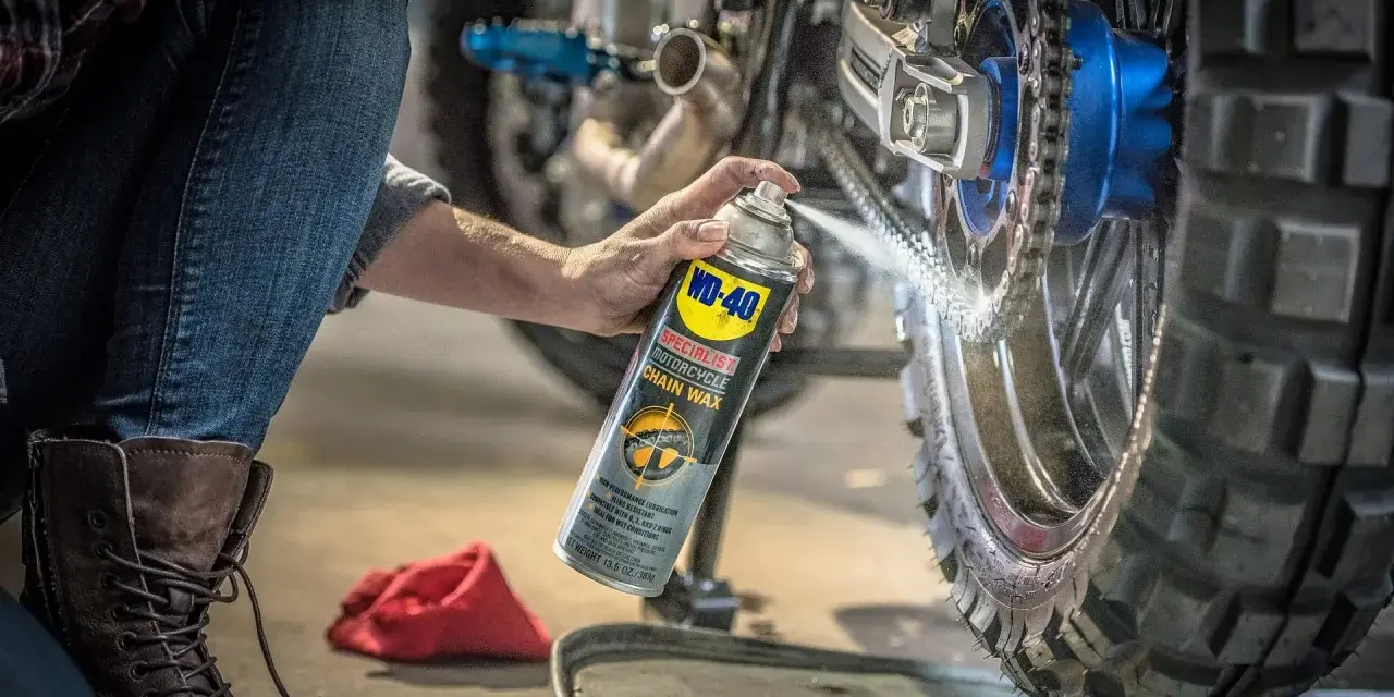 Persona en cuclillas aplica cera a la cadena de una moto. Mantenimiento esencial para engrasar cadena moto y asegurar un viaje suave.