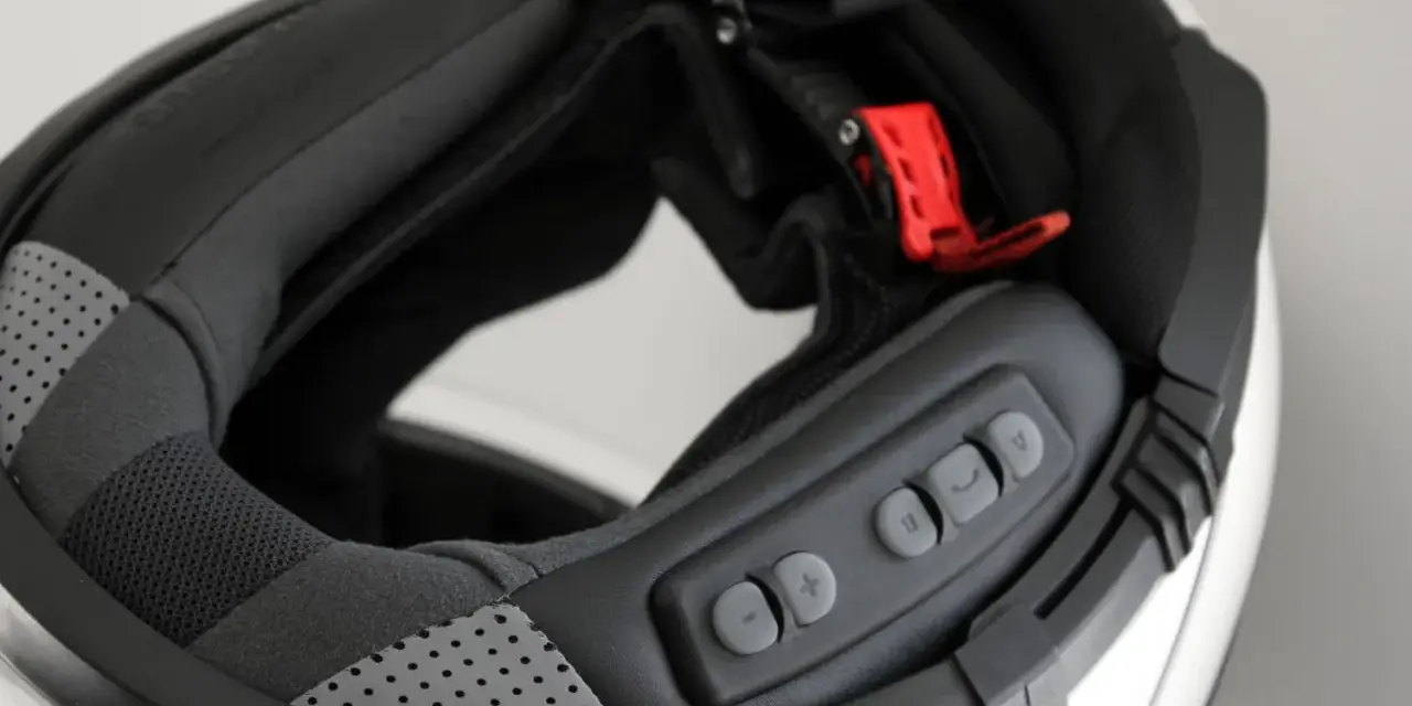 Detalle del interior de un casco modular, mostrando el proceso para instalar intercomunicador. Botones de control visibles.