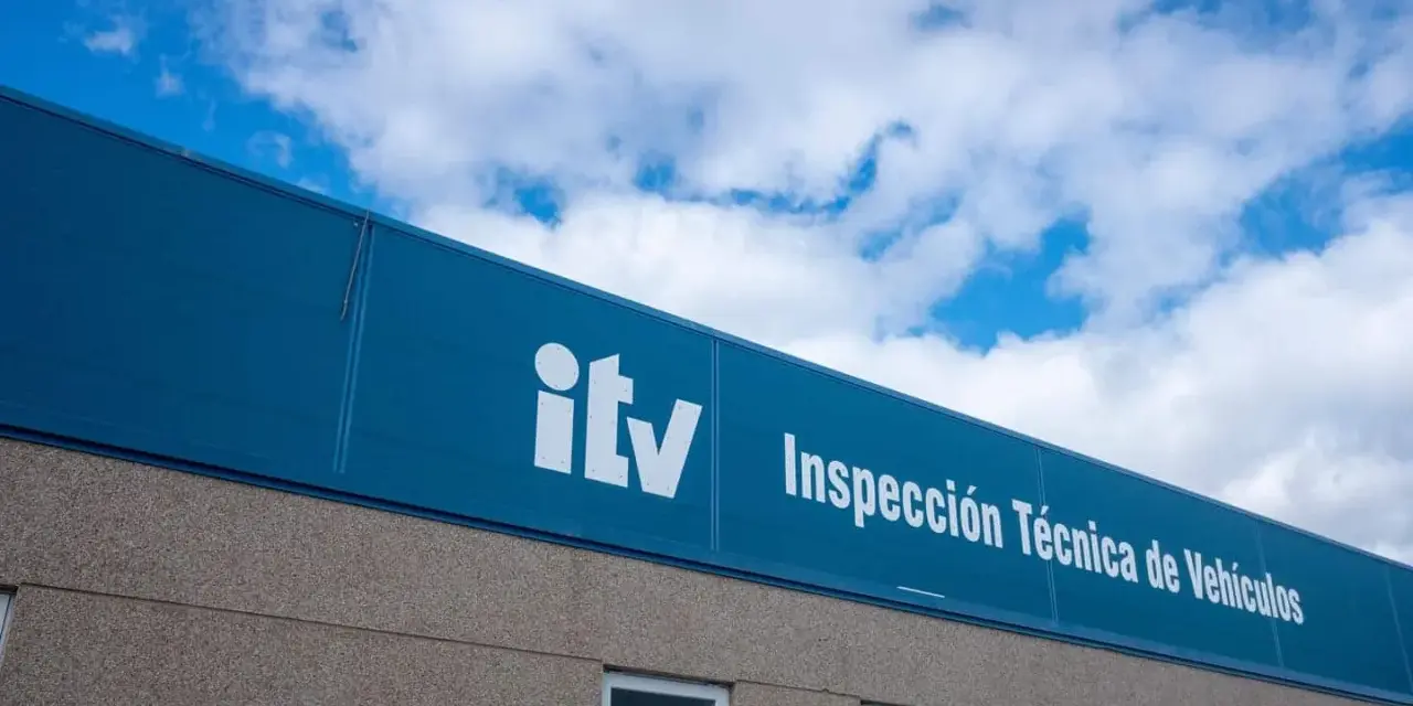 Edificio de la ITV bajo un cielo azul con nubes. El letrero blanco dice "itv Inspección Técnica de Vehículos".
