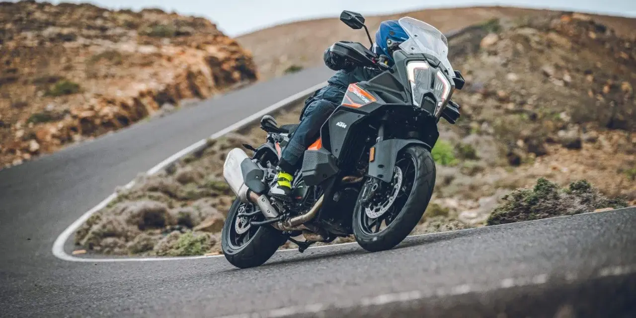 Motociclista en una KTM 1290 Adventure, inclinada en una curva de carretera montañosa. El peso de la moto se siente en la maniobra.