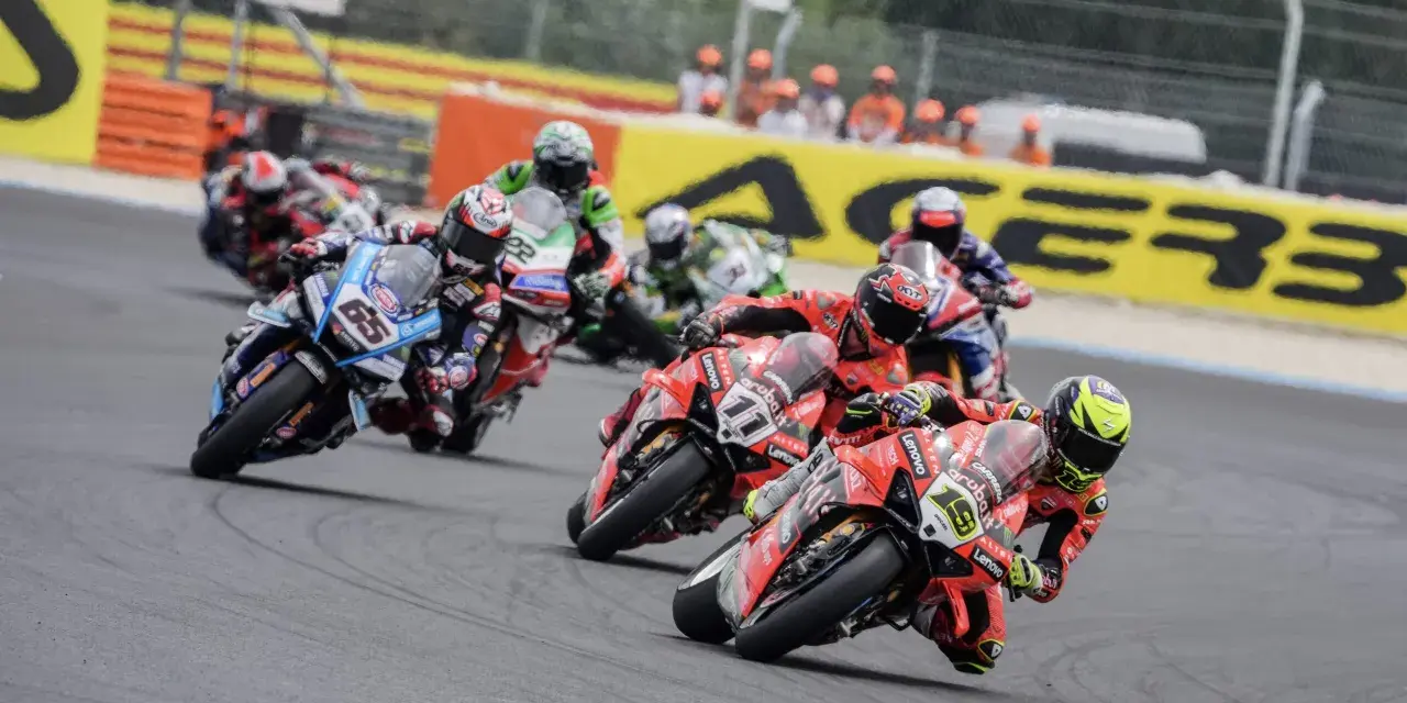 Motociclistas compiten en una carrera, con el número 65 en primer plano. El sbk calendario se acerca.