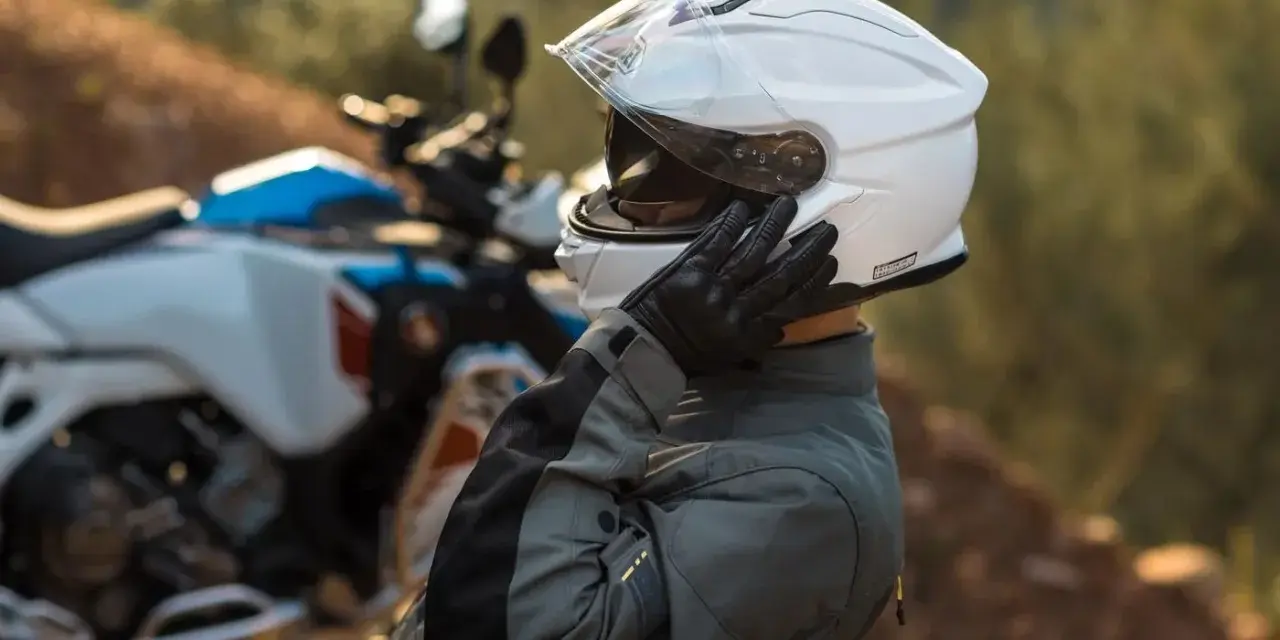 Motociclista ajustándose su casco modular silencioso blanco, listo para la aventura.