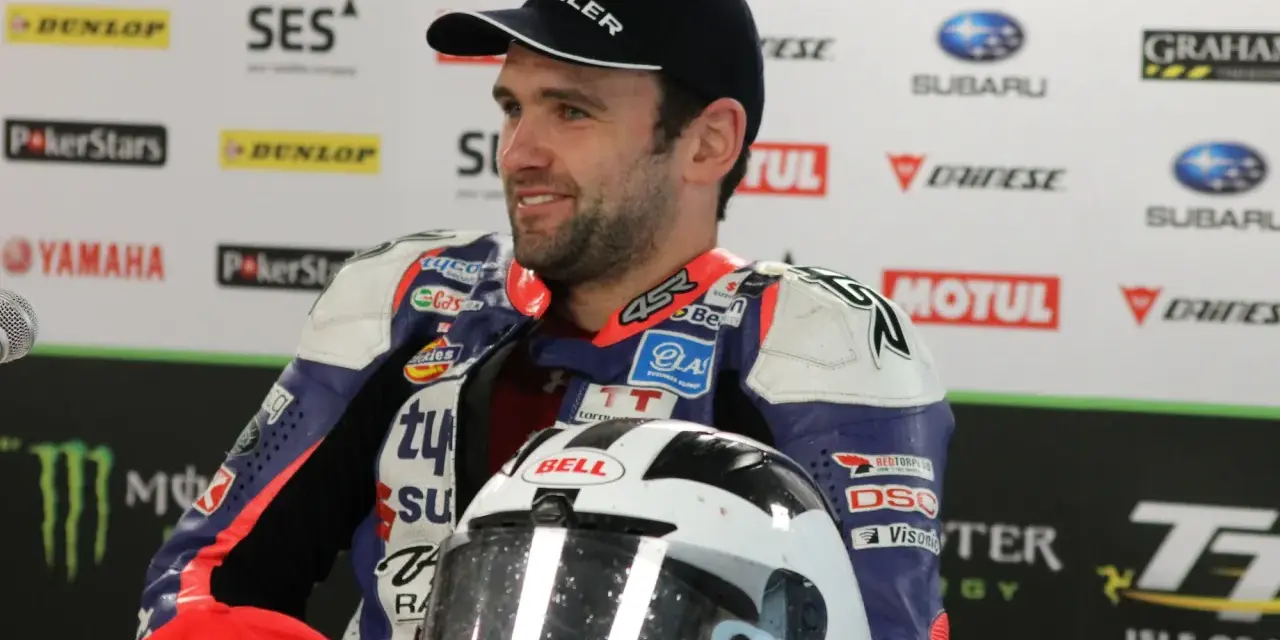 William Dunlop, piloto de motociclismo, sonríe con su casco de carreras y mono de competición.
