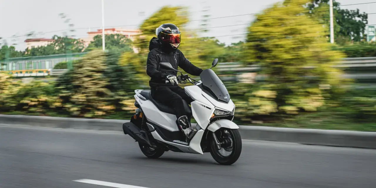 Persona conduce moto blanca con carnet B, disfrutando del paisaje borroso.