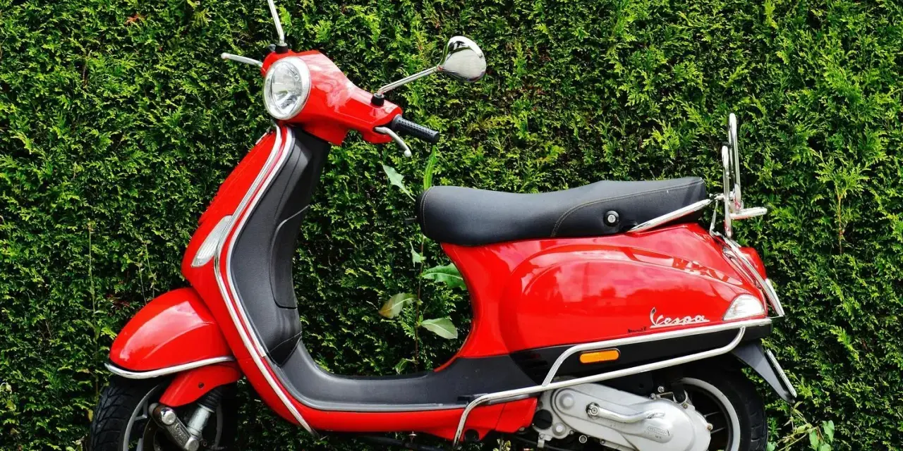 Scooter roja aparcada frente a un seto verde. Ideal para entender las diferencias carnet a1 y a2.