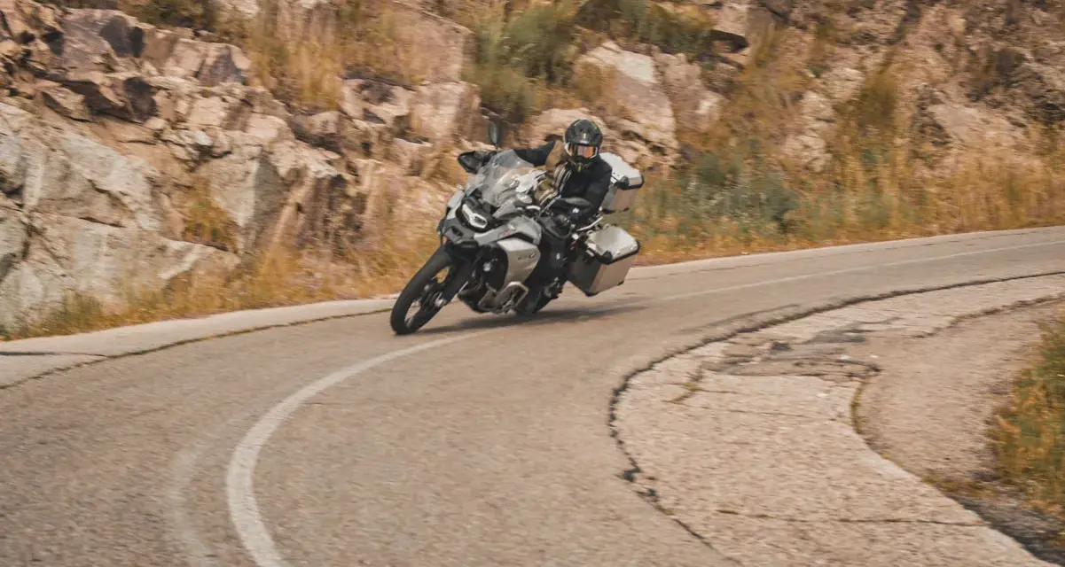 Motociclista en pruebas de motos, inclinado en una curva de carretera montañosa.