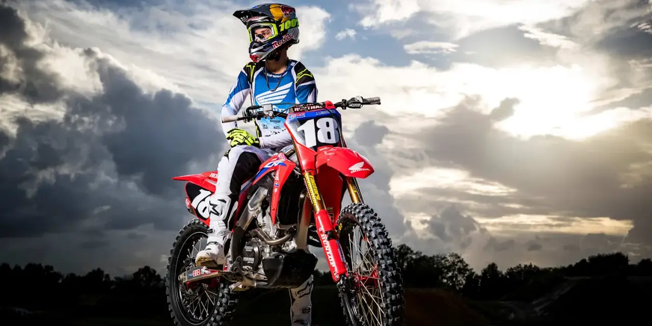 Jett Lawrence, piloto de motocross, posa con su moto roja bajo un cielo dramático.