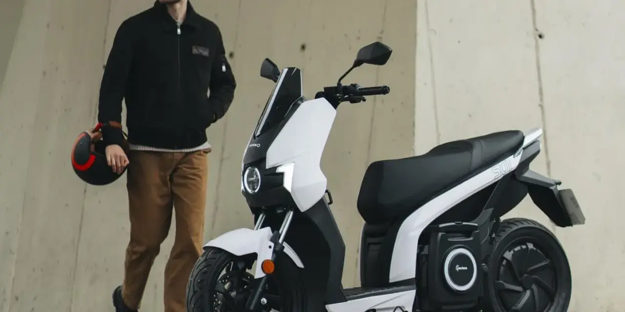 Hombre con casco junto a un scooter eléctrico blanco, el scooter mas potente para la ciudad.