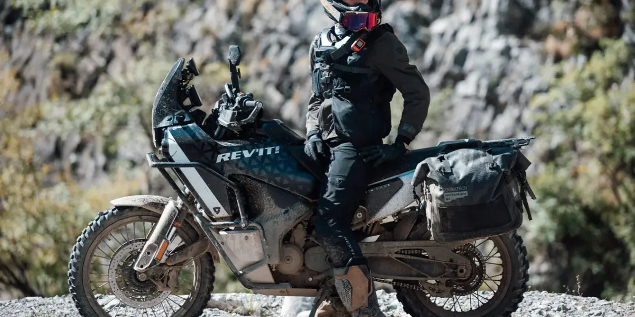 Motociclista con chaqueta REV'IT! y equipo de aventura, listo para aprender como lavar chaqueta de moto después de un viaje polvoriento.