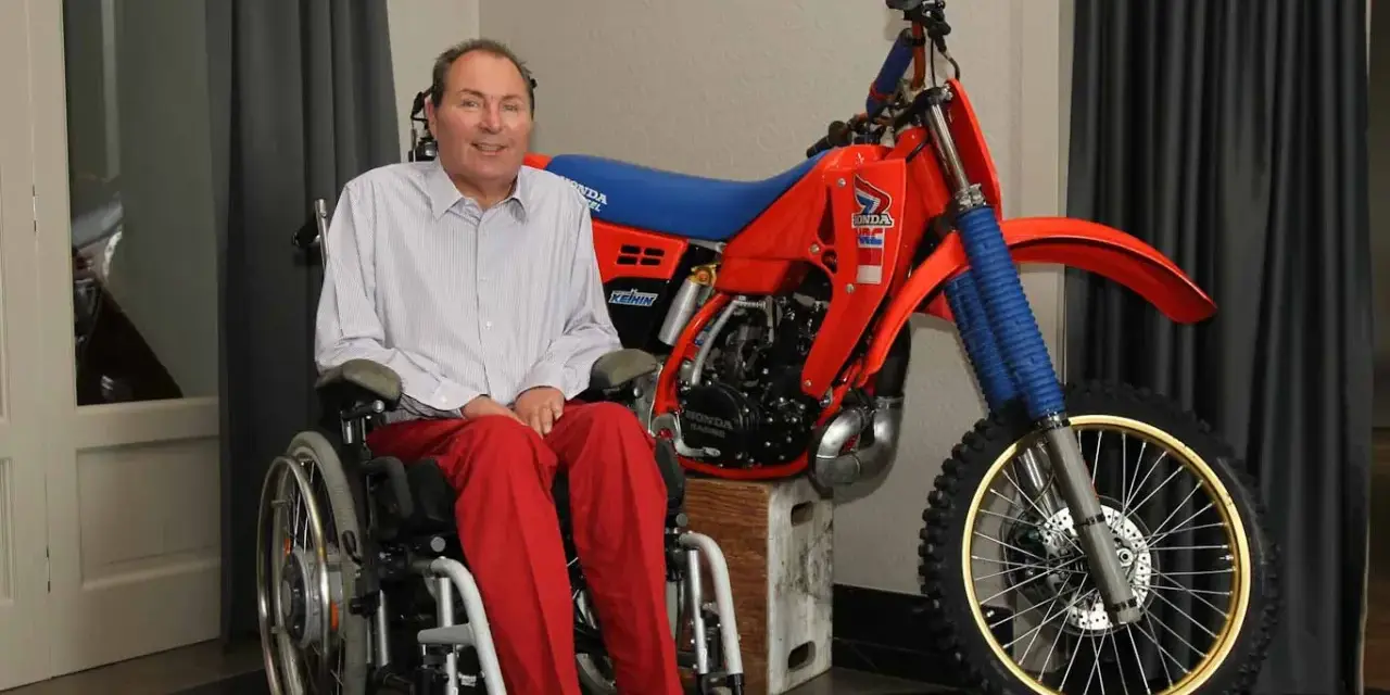 Andre Malherbe, leyenda del motocross, sonríe junto a su icónica moto Honda roja.