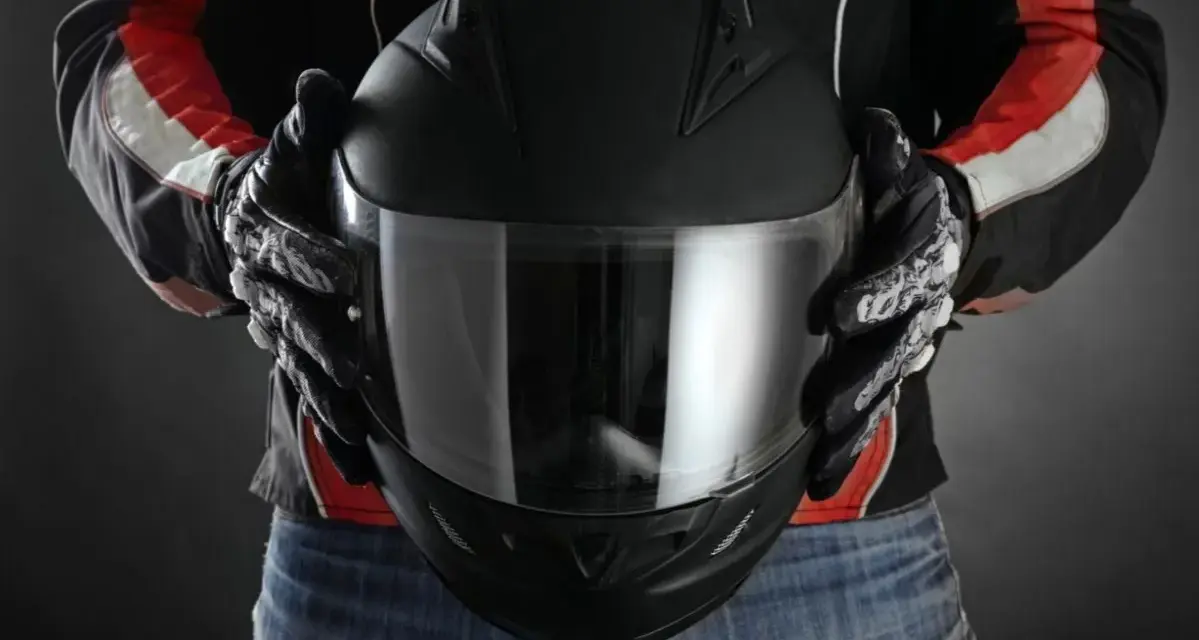 Persona con guantes de moto sostiene casco negro. Se aprecian detalles de las medidas exteriores casco moto en su diseño.