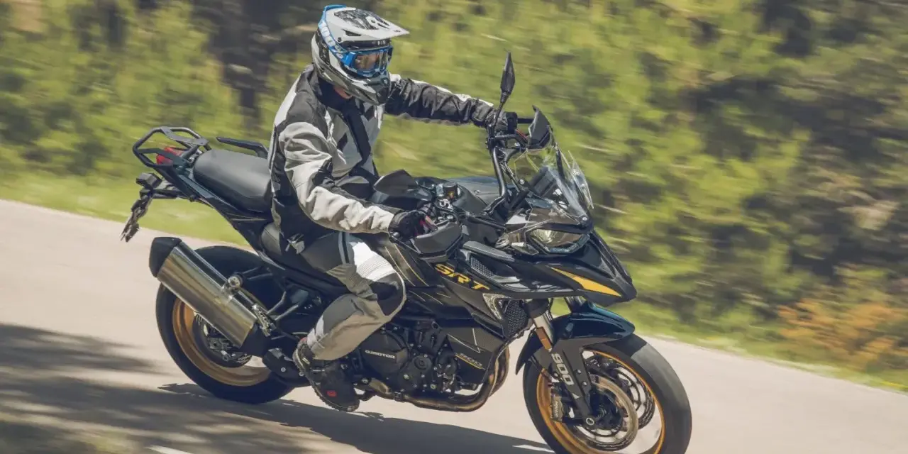 Motociclista con equipo de protección conduce una de las motos trail media cilindrada por una carretera rodeada de vegetación.