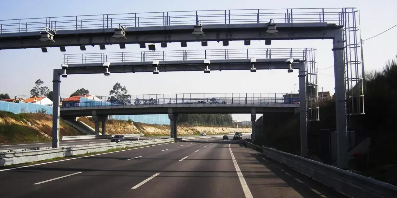 Un pórtico de peaje automático en España. Los coches circulan por la autopista bajo una estructura metálica con antenas.