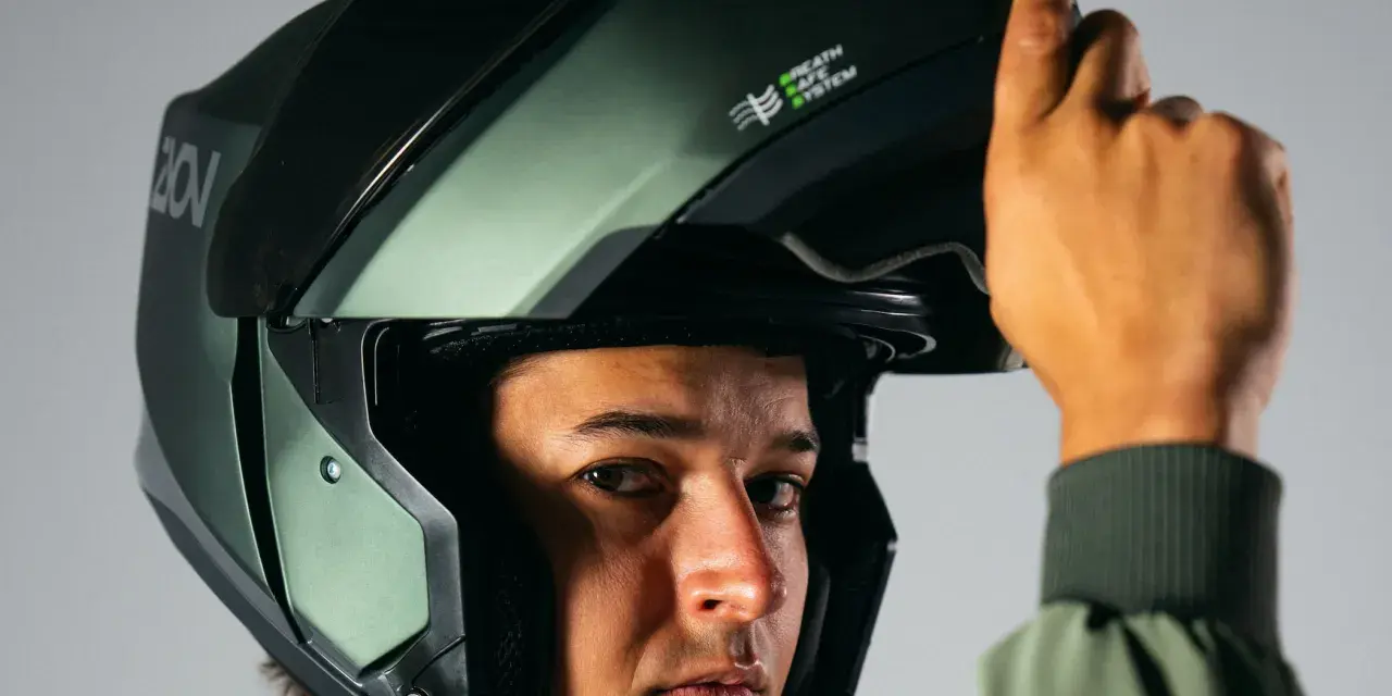 Hombre ajustando su casco integral o modular, de color verde militar, con sistema de ventilación.