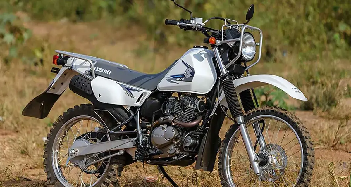 Suzuki DR 200 lista para la aventura. Moto blanca de doble propósito con neumáticos todoterreno, lista para explorar caminos rurales.