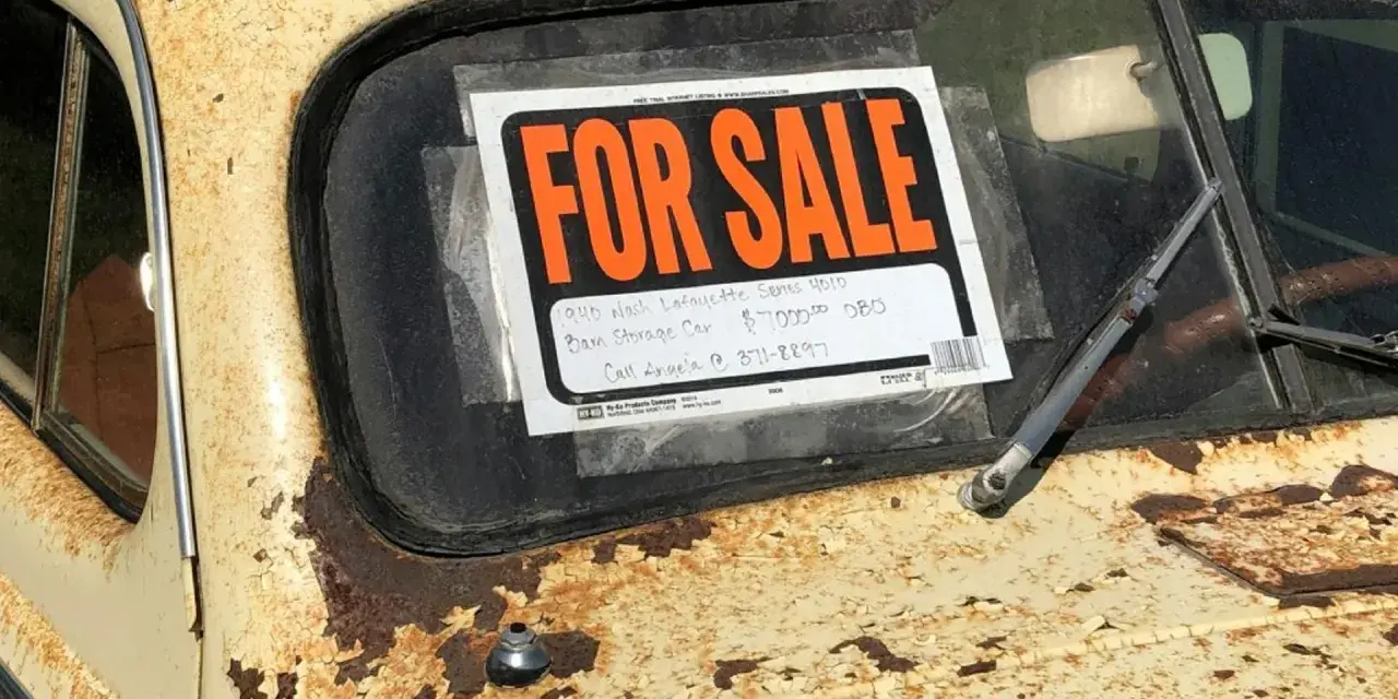 Coche antiguo a la venta, con cartel "FOR SALE". Para saber si una moto tiene cargas, revisa su historial.