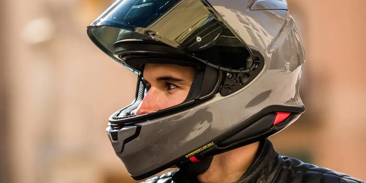 Hombre con casco de moto gris brillante. ¿Cuánto pesa un casco de moto? Este modelo parece ligero y aerodinámico.