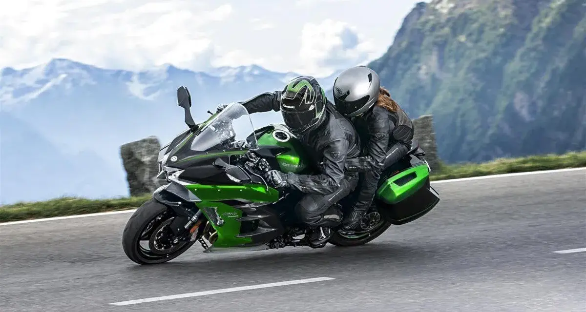 Pareja en una moto deportiva verde y negra, disfrutando de un viaje por carretera entre montañas. ¡Las mejores motos deportivas para aventuras!
