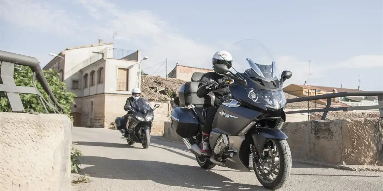 Dos motociclistas en sus Benelli 1200 GT recorren un pueblo soleado.
