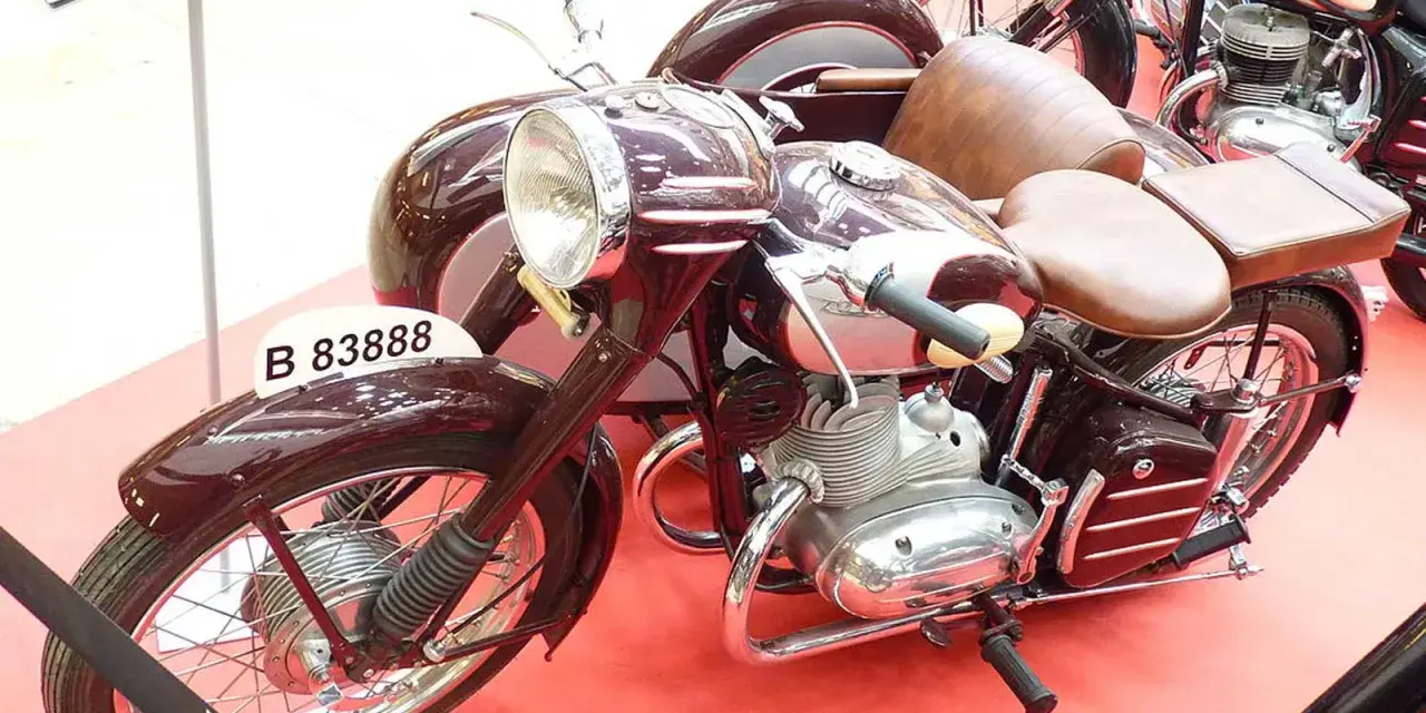 Moto Derbi clásica con sidecar, color burdeos, con asientos de cuero marrón y detalles cromados.