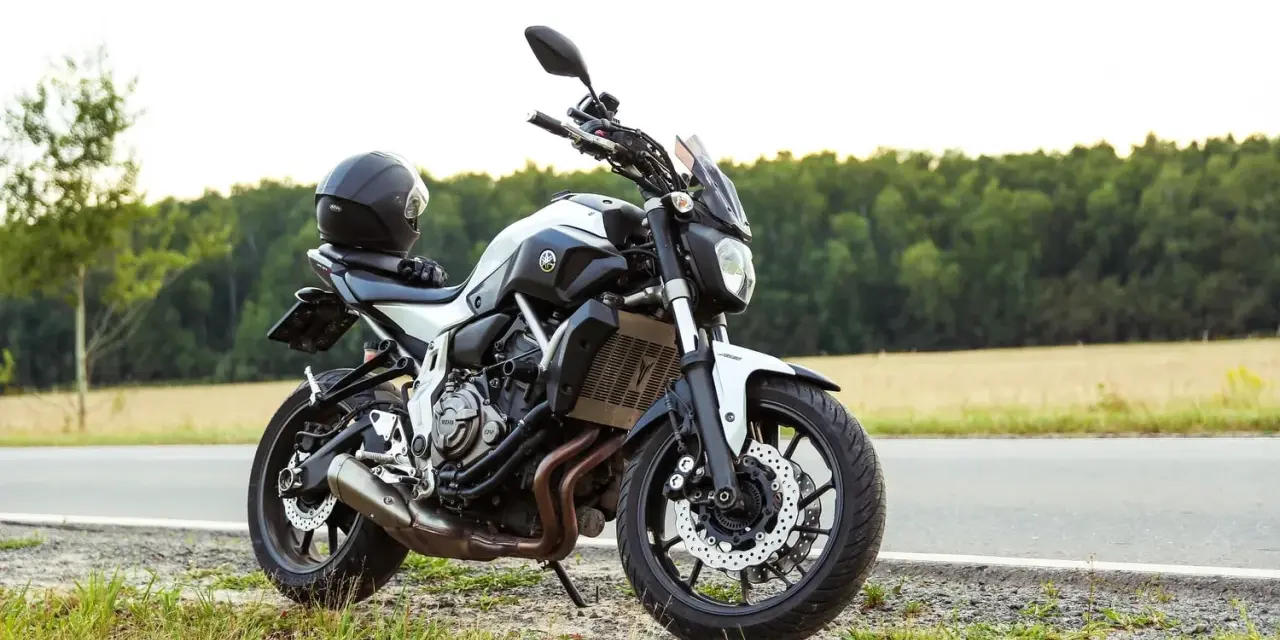 Una moto a2 blanca y negra, con un casco negro en el asiento, aparcada en la cuneta de una carretera rural.