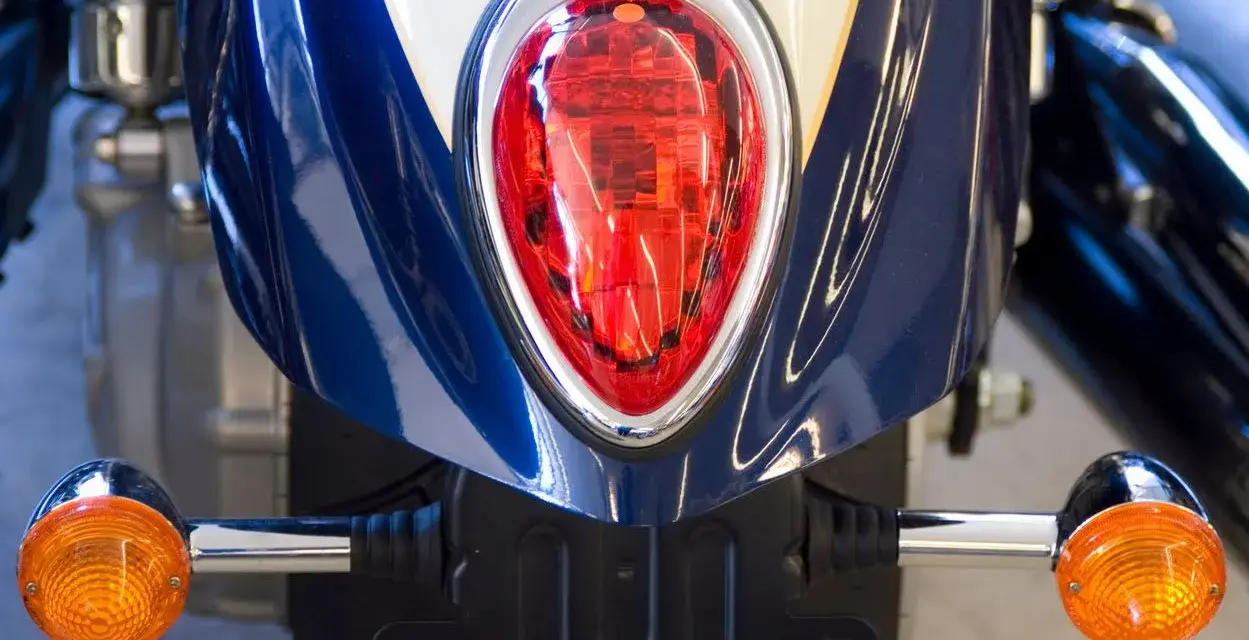 Detalle de la parte trasera de una moto azul y blanca, con intermitentes naranjas y luz roja. Podría ser una multa por llevar luces led moto.