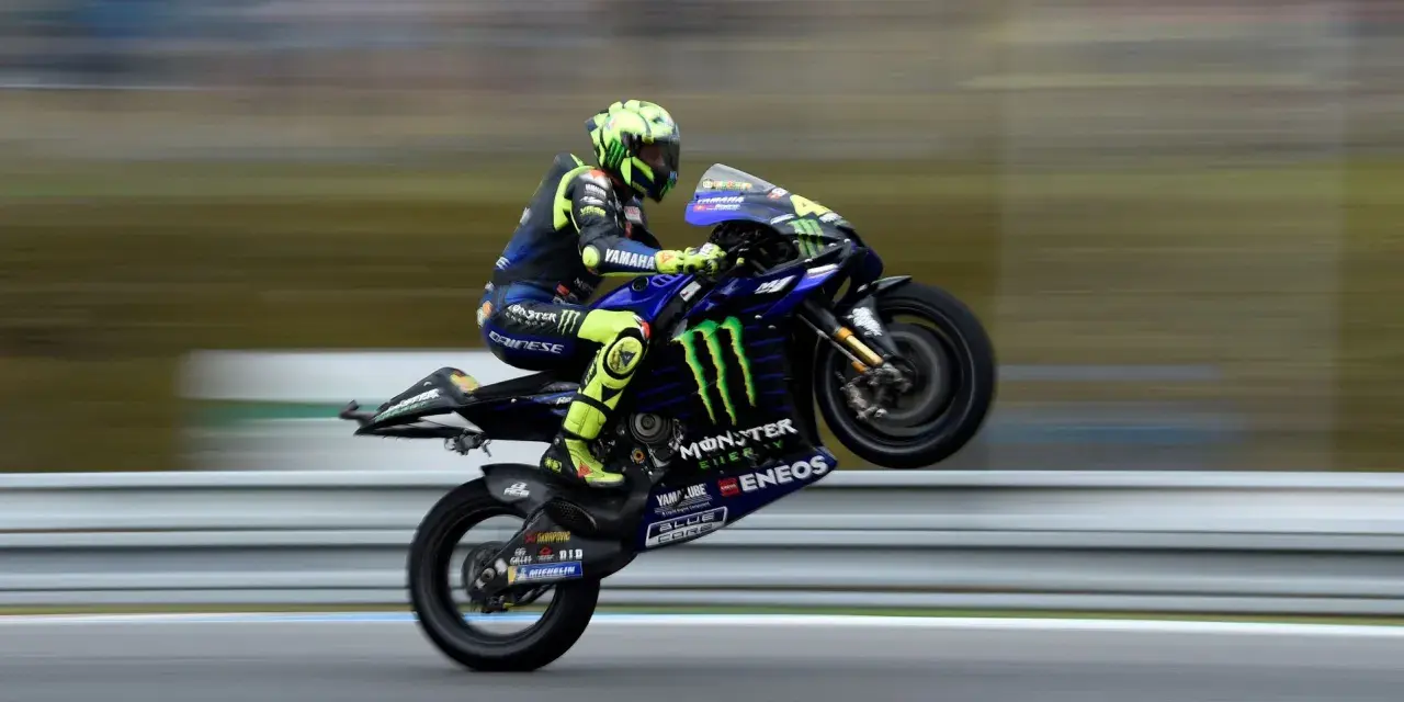 Valentino Rossi levanta la rueda trasera de su Yamaha en plena carrera, con su icónico casco amarillo y traje azul.