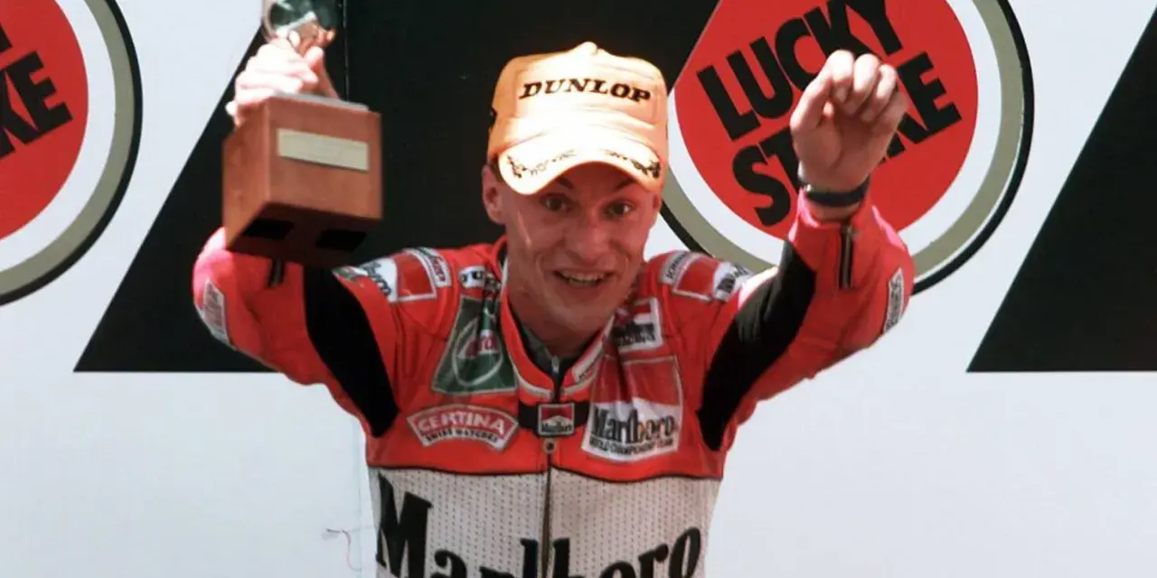 Ralf Waldmann, piloto de motos, celebra con un trofeo y un puño en alto, luciendo su traje de competición Marlboro.
