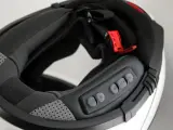 Detalle del interior de un casco modular, mostrando el proceso para instalar intercomunicador. Botones de control visibles.